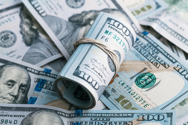 Un rotolo di noi banconote da cento dollari che giacciono su un mucchio di contanti dagli Stati Uniti d'America
