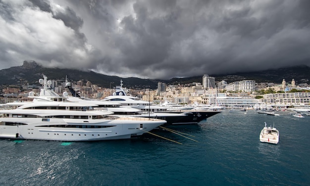 Un sacco di enormi yacht sono nel porto di monaco durante la tempesta, la montagna è sullo sfondo del bordo lucido o...