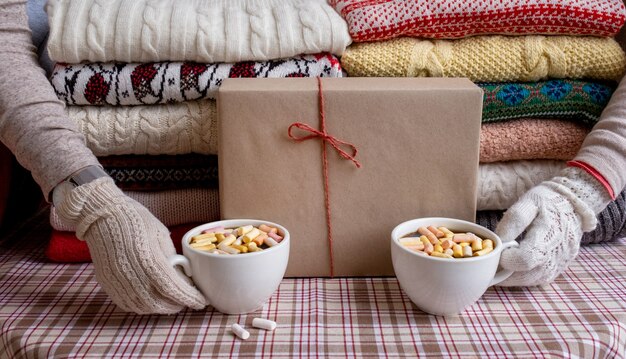 Un sacco di maglioni e pullover di diversi colori piegati in due pile e mani con due tazze di caffè.