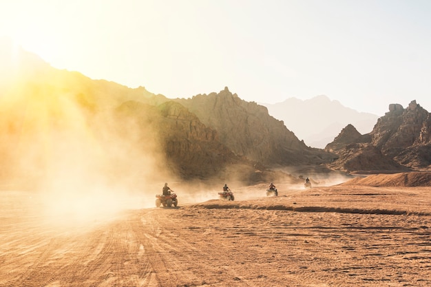 Un sacco di quad nella polvere cavalcano sullo sfondo del deserto selvaggio. Tramonto nel deserto oltre le montagne. Raduno di quad. Gruppo di turisti su ATV nel deserto egiziano.