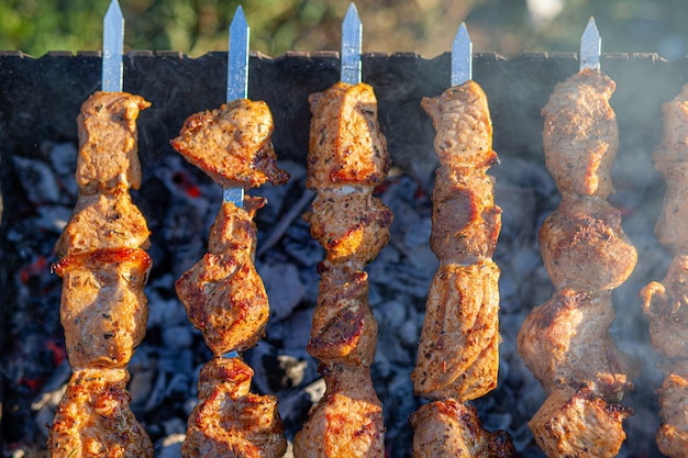 Un sacco di spiedini di carne succosi di fila alla griglia. Pezzi di carne infilati su spiedini di metallo alla griglia al tramonto. Il processo di cottura degli spiedini con molto fumo. Cucinare nella natura