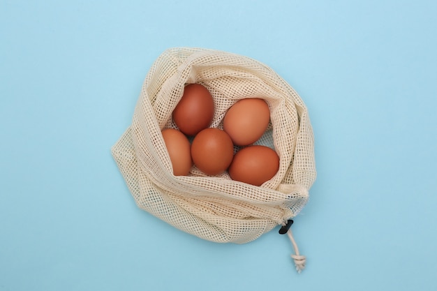 Un sacco di uova di gallina in sacchetto di cotone ecologico su sfondo blu pastello. Vista dall'alto