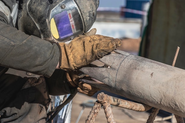 Un saldatore in abiti da lavoro sta saldando un tubo in un cantiere edile. Avvicinamento.