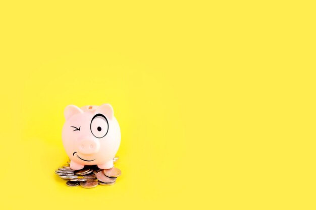 Un salvadanaio sorridente su Mucchio di monete su sfondo giallo Risparmio e crisi dei prestiti S