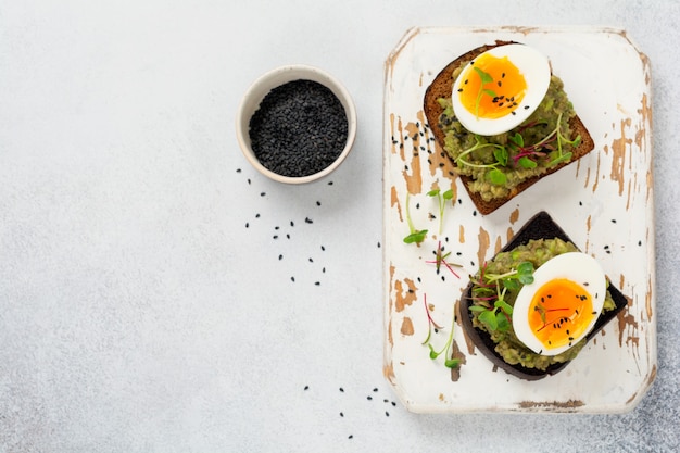 Un sano panino con avocado, uova e microgreens su pane tostato su un piatto da portata