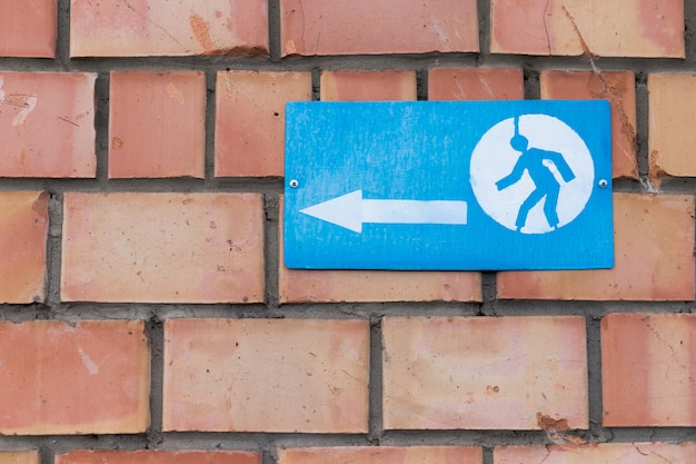 Un segno con un segno di freccia e un uomo che correva avvitato a un muro di mattoni.