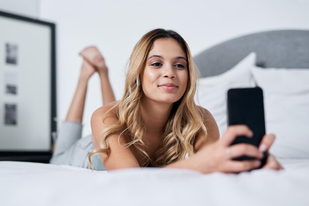 Un selfie al giorno tiene a bada la noia Inquadratura di una giovane donna che usa il cellulare mentre è sdraiata sul letto