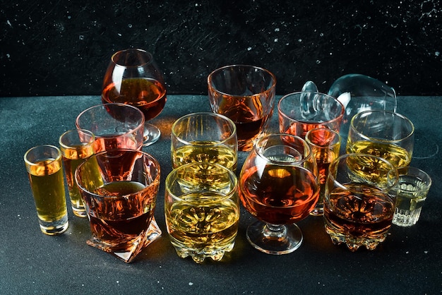 Un set di bicchieri con varie bevande alcoliche vodka cognac tequila scotch brandy e whisky grappa liquore vermouth tintura rum forti bevande alcoliche su uno sfondo di pietra