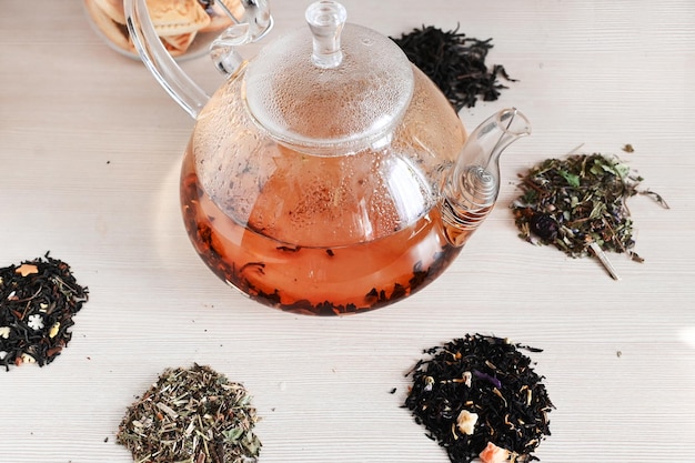 Un set di diversi tipi di tè accanto al bollitore riempito di tè caldo su uno sfondo beige