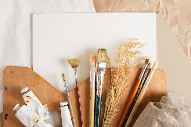 Un set di pennelli, una tavolozza di legno, tela bianca su cartone e carta su uno sfondo di lino, concetto di officina dell'artista