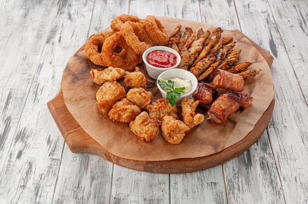 Un set di snack per birra a base di frutti di mare. Spratto fritto, filetto di pollock, anelli di calamaro Con salsa di pomodoro e formaggio. Su una tavola di legno rotonda. Fondo in legno chiaro. Vista dall'alto.