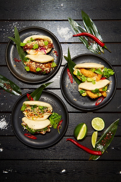 Un set di tre piatti asiatici su piatti neri su un tavolo di legno decorato con lime, peperoncino e farina. Bao appetitoso con verdure e carne