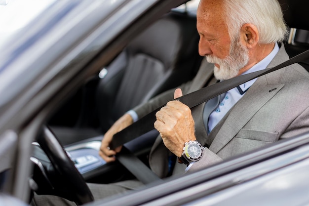 Un signore anziano che si allaccia la cintura nella sua auto di lusso prima di una corsa