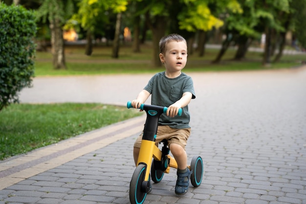 Un simpatico bambino di due o tre anni va in bicicletta o in equilibrio in un parco cittadino in una soleggiata giornata estiva Concetto di infanzia e infanzia Messa a fuoco selettiva