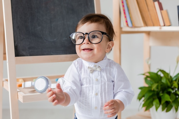 Un simpatico ragazzino con gli occhiali che sorride accanto alla lavagna e ai libri. educazione prescolare per bambini