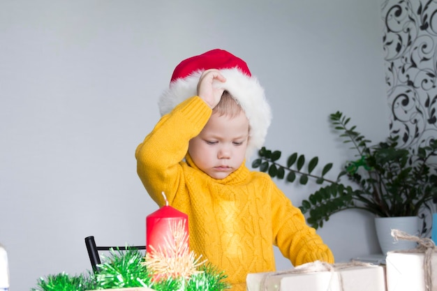 Un simpatico ragazzino con un maglione giallo si toglie il cappello rosso di Babbo Natale