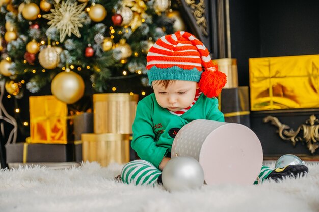 Un simpatico ragazzino vestito da elfo apre un regalo di Natale in una casa di Natale decorata.