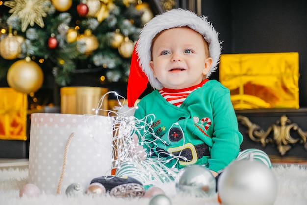 Un simpatico ragazzino vestito da elfo apre un regalo di Natale in una casa di Natale decorata.