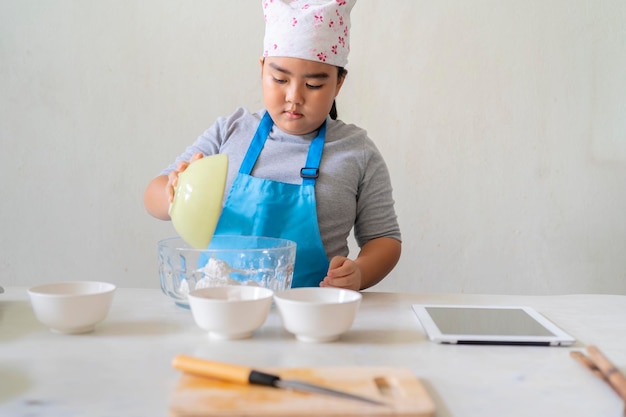 Un simpatico ragazzo asiatico sta imparando i dolci, sta versando gli ingredienti insieme Nella cucina di casa Una ragazza asiatica sta imparando a cucinare
