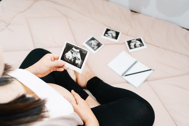 Un simpatico ventre incinta e una scansione a raggi x di un bambino asiatico giovane donna incinta rilassarsi nella stanza guardando la sua immagine del bambino nelle mani dolce concetto di maternità terzo trimestre