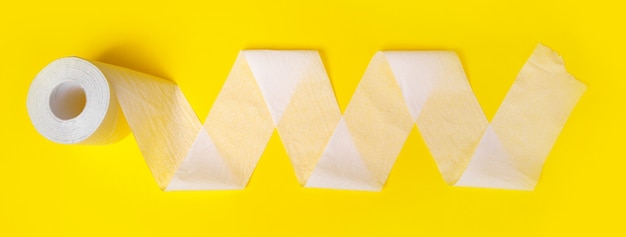 Un singolo rotolo di carta igienica srotolato su sfondo giallo, immagine panoramica
