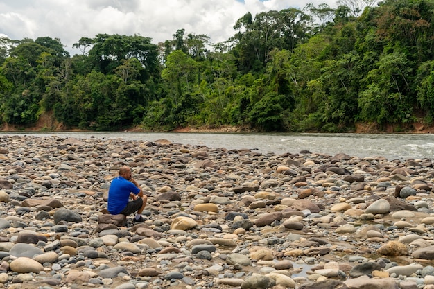 Un solo uomo seduto sul bordo del fiume nella giungla amazzonica, Ecuador,