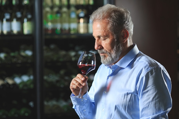 Un sommelier anziano sta assaggiando il vino rosso.