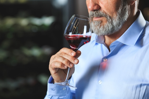 Un sommelier anziano sta assaggiando il vino rosso.