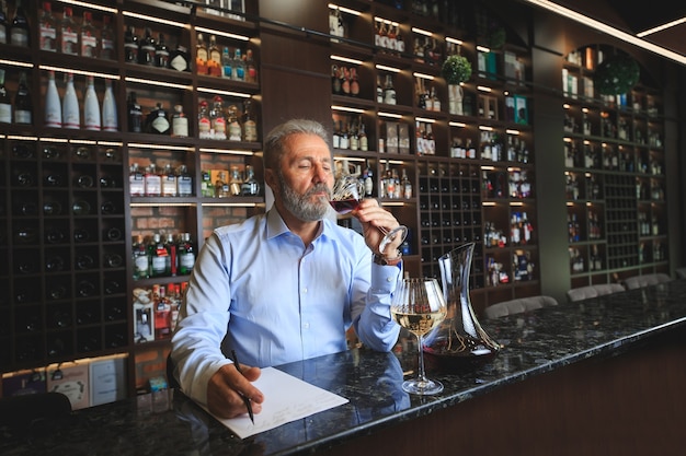 Un sommelier anziano sta assaggiando il vino rosso.