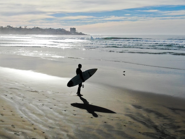 Un surfista si trova sulla spiaggia con la sua tavola da surf di fronte a una città.