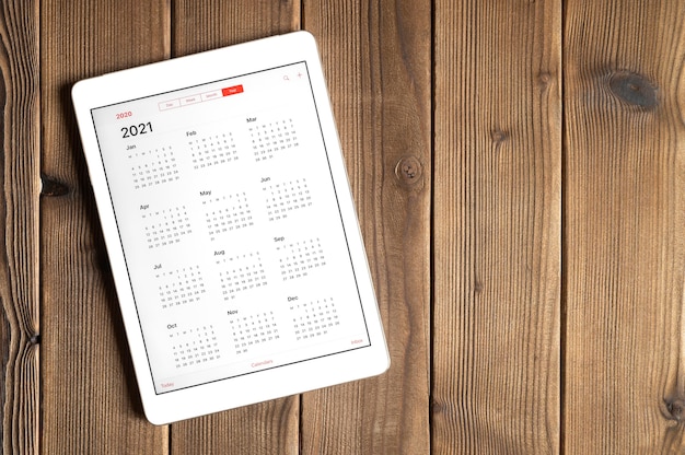 Un tablet con un calendario aperto per l'anno 2021 su uno sfondo di tavola di assi di legno. spazio per il testo