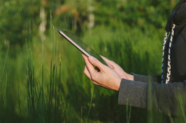 Un tablet nelle mani di un primo piano della ragazza. sullo sfondo della natura verde.