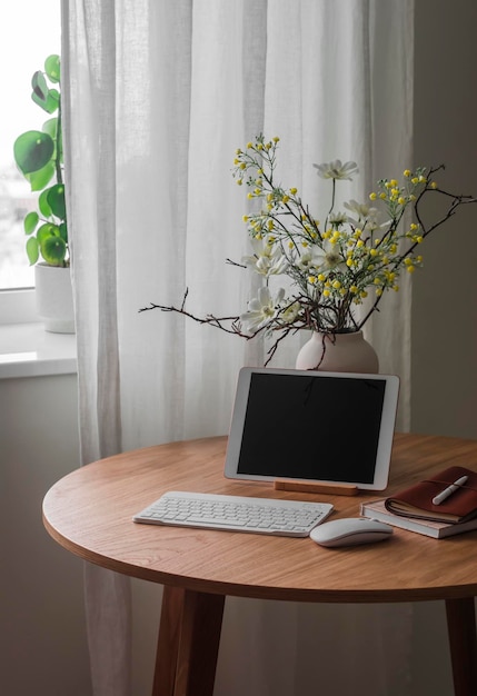 Un tablet una tastiera un vaso di fiori su un tavolo di legno rotondo vicino alla finestra nel salotto