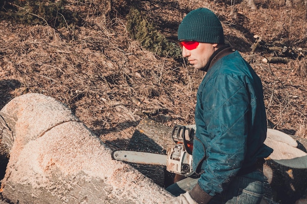 Un taglialegna taglia un albero con una motosega che prepara legna da ardere per l'inverno