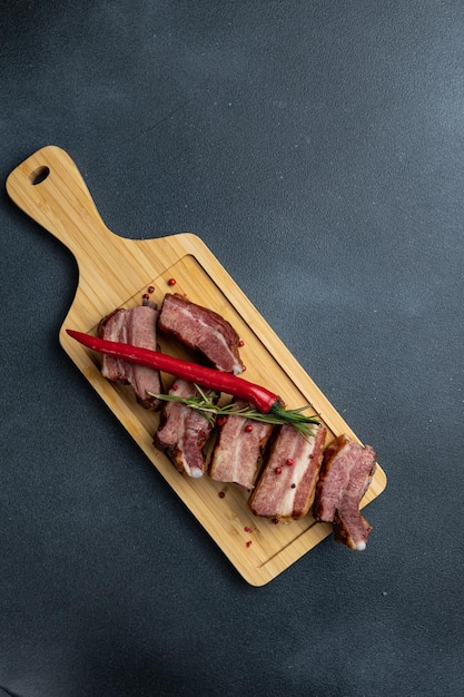 Un tagliere di legno con carne affettata e un peperone rosso sopra.