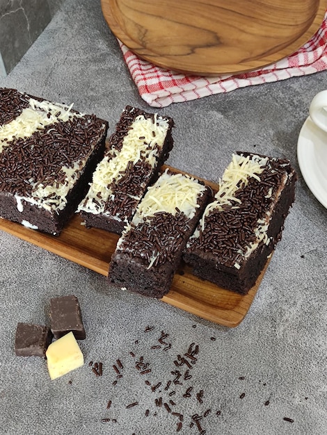 Un tagliere di legno con sopra una torta e delle codette di cioccolato.