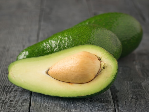 Un taglio e due interi avocado sul tavolo rustico in legno.