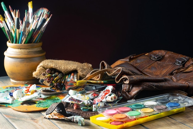 Un tavolo pieno di materiale artistico tra cui un sacchetto di vernice, una borsa, una borsa, una borsa e un sacchetto di vernice.