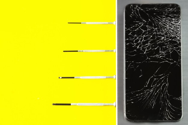 Un telefono rotto con un display rotto e cacciaviti su uno sfondo giallo-grigio