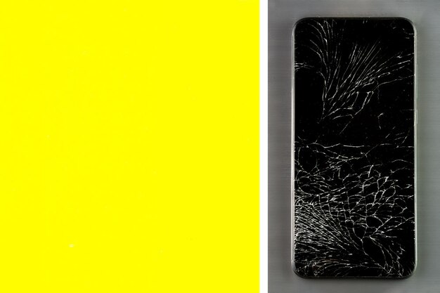 Un telefono touch con uno schermo rotto giace su una superficie spazzolata in metallo grigio Layout con spazio per copiare il colore giallo