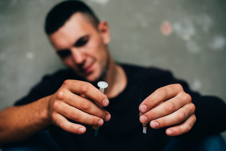 Foto un tossicodipendente con una siringa in mano e una sigaretta tra i denti è seduto per terra dopo...