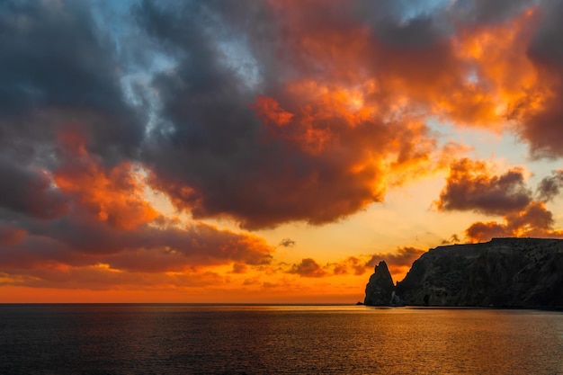 Un tramonto infuocato d'oro con la silhouette di un promontorio roccioso sulla spiaggia del mare oceano estivo mare
