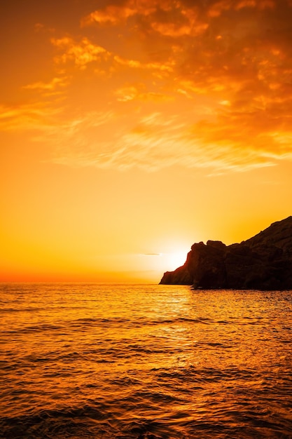 Un tramonto rosso ardente sul mare con scogliera rocciosa vulcanica natura astratta estate o oceano primaverile