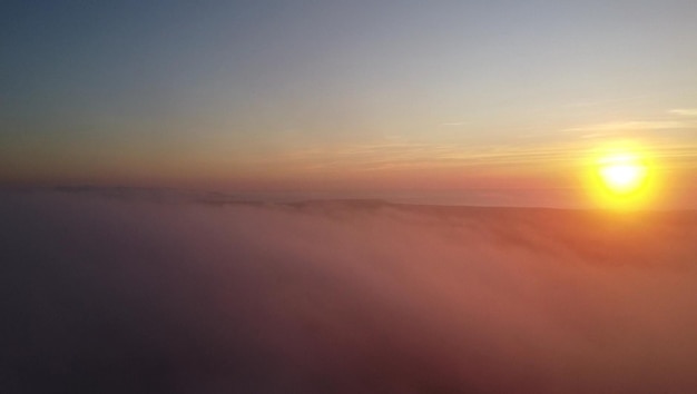 Un tramonto su un paesaggio nebbioso con un cielo rosa e il sole tramonta dietro le nuvole.