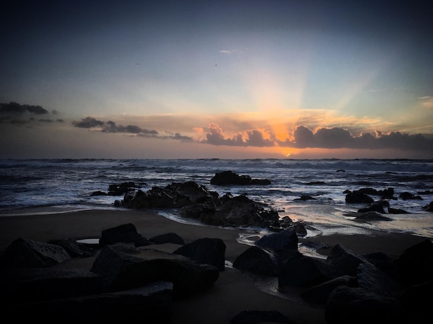 Un tramonto sull'oceano con rocce e nuvole.