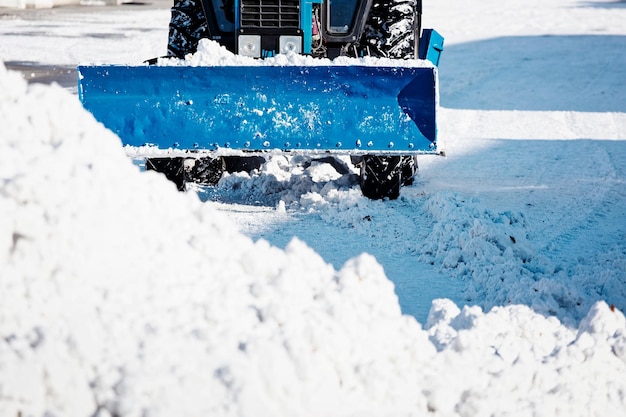 Un trattore blu con una pala pulisce le strade dalla neve in una soleggiata giornata invernale