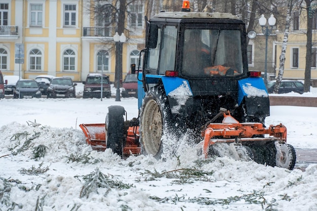 Un trattore pulisce la neve in città in inverno dopo una nevicata Pulizia delle strade della città dalla neve Autista del trattore al lavoro nella piazza della città durante una tempesta di neve