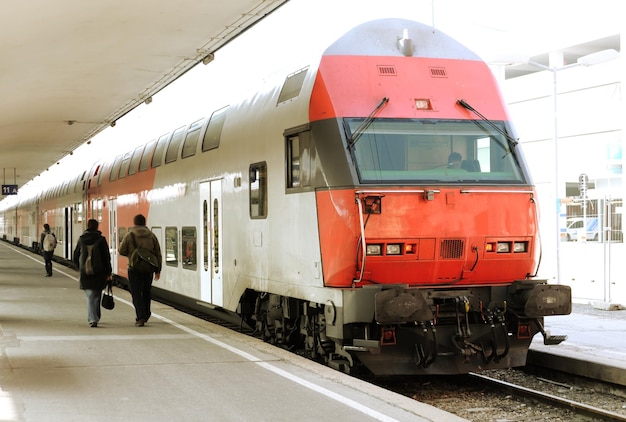 Un treno è fermo in una stazione con gente che passa.