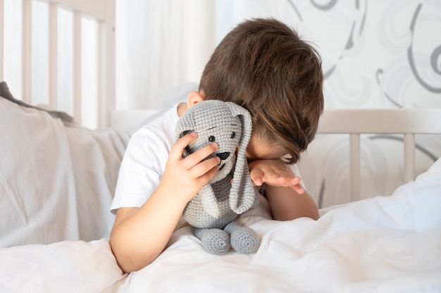 Un triste bambino di tre anni seduto sul letto e piangendo. Il ragazzo ha fatto un brutto sogno. Foto di alta qualità