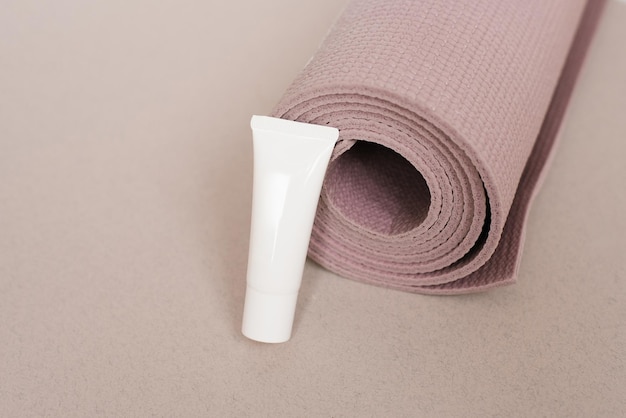 Un tubo bianco di crema giace accanto ai tappetini rosa dello yoga.